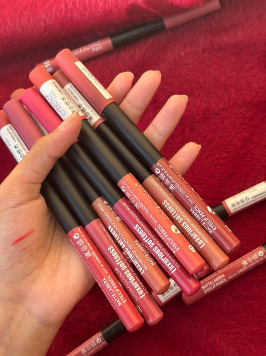 A hand holding multiple Emellie matte lip liners in different nude and pink tones over a soft red textured cloth.