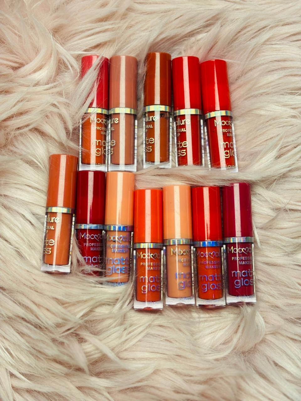 Twelve Mocallure matte and gloss lipsticks arranged on a soft fur surface, showing various nude and bold colors.