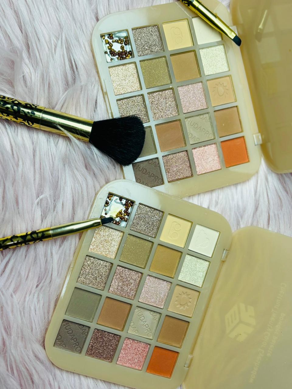 Huda Pro 20 Color Eyeshadow Palette with matte, shimmer, and glitter shades displayed open with makeup brushes on a soft textured background.
