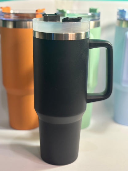 Black insulated mug with a handle on a white surface, surrounded by other colorful mugs.