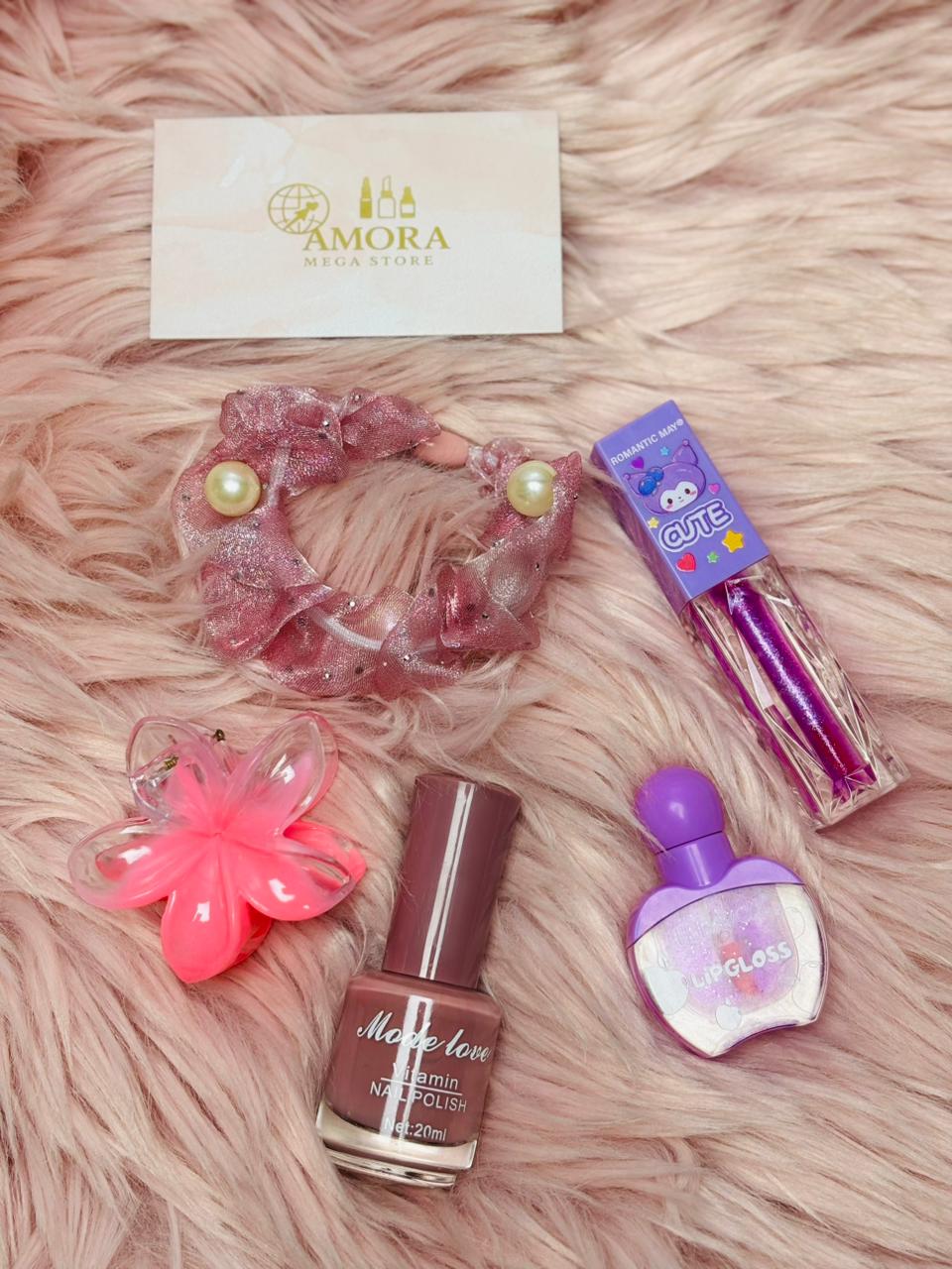 Flat lay of a pink-themed beauty kit including nail polish, lip gloss, hair scrunchie, flower clip, and Amora Mega Store card on a soft furry background.