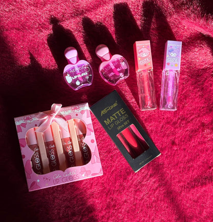 A collection of assorted lip gloss sets including heart-shaped glosses, cartoon-tube glosses, a pink gift box gloss set, and a matte lip gloss trio, all arranged on a bright red furry background.