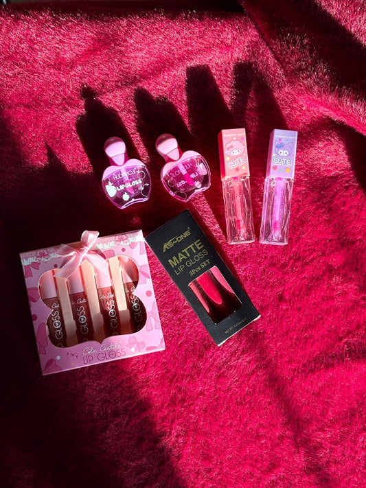 A collection of assorted lip gloss sets including heart-shaped glosses, cartoon-tube glosses, a pink gift box gloss set, and a matte lip gloss trio, all arranged on a bright red furry background.