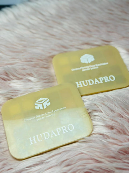 Two yellowHUDAPRO eyeshadow pans on a pink fur background