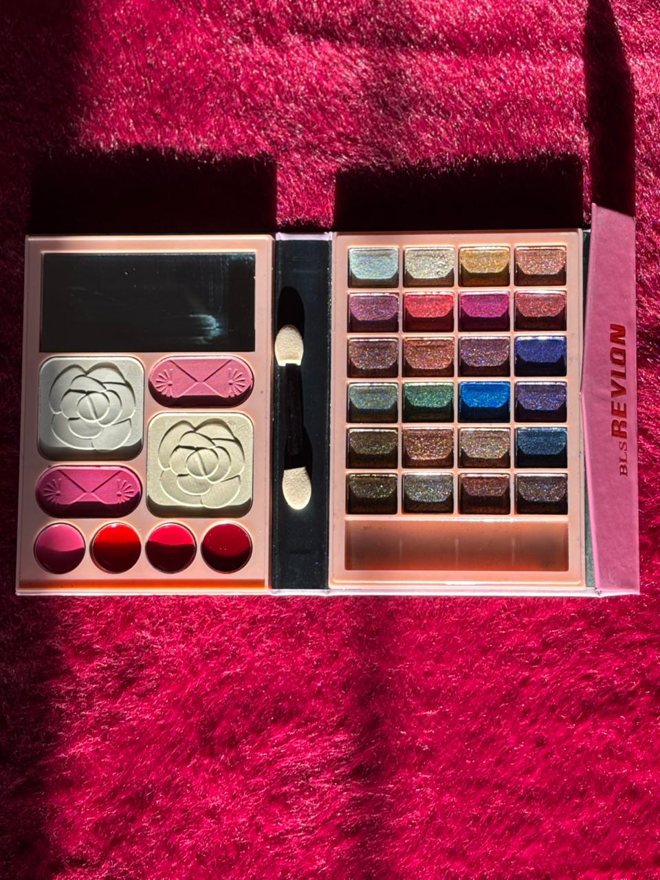 An open makeup palette with bright eyeshadow shades, blushes, and lip colors arranged neatly on a red furry background.