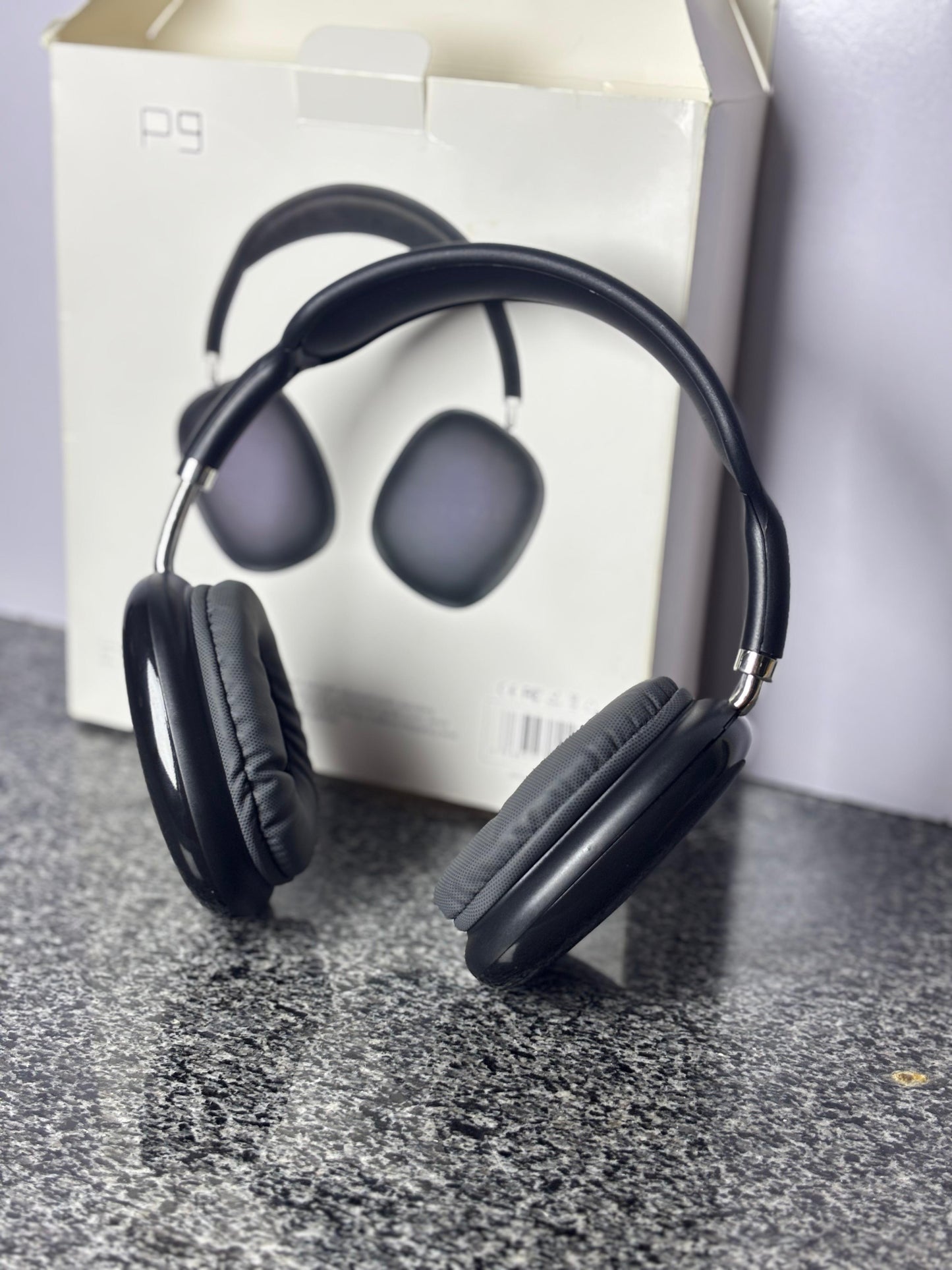Black Bluetooth headphones displayed upright in front of their original box on a dark surface.