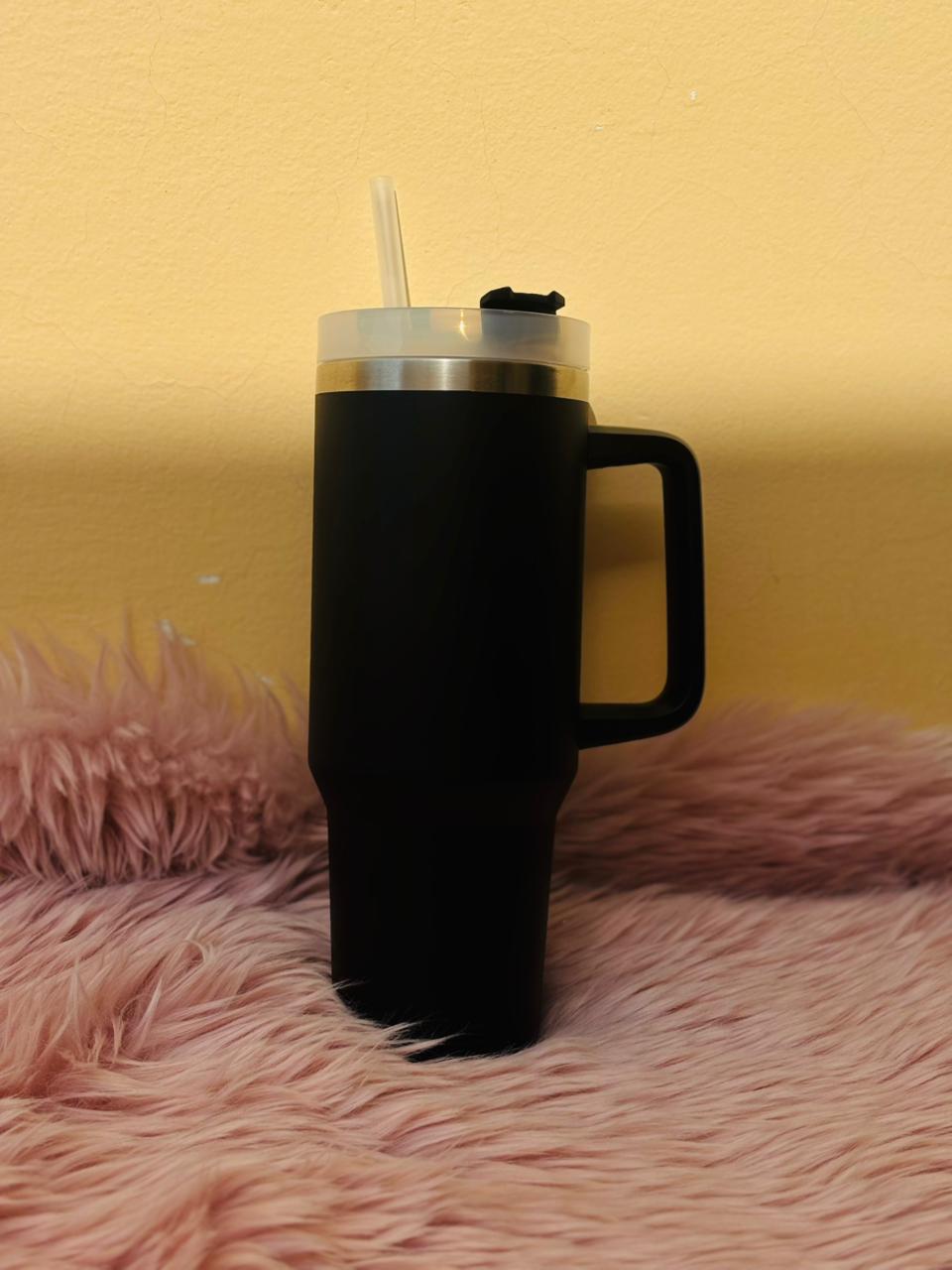 Black matte insulated tumbler cup with handle and straw placed on a soft pink fur surface for a cozy aesthetic.