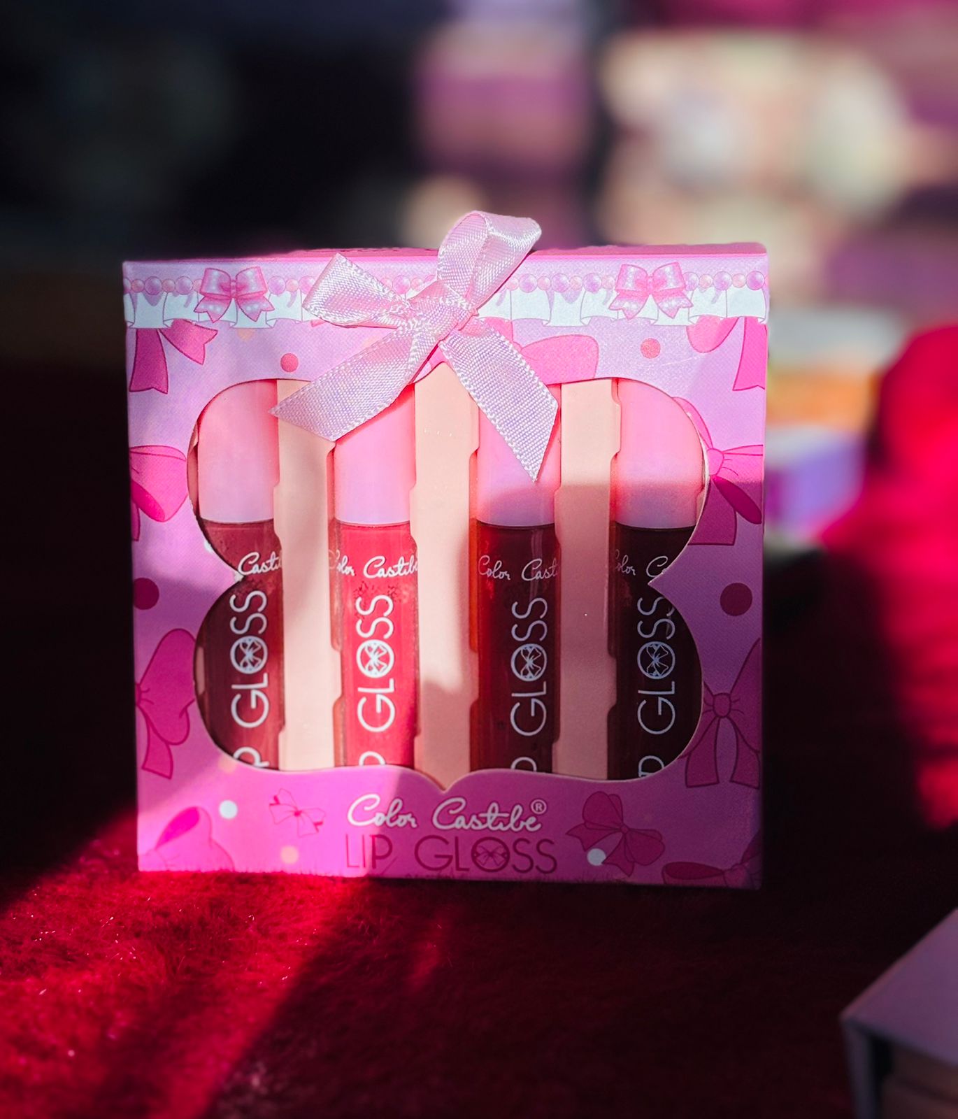 A pink box containing 4 Color Castle lip gloss tubes, each visible through butterfly-shaped cutouts, with a small decorative ribbon on top.