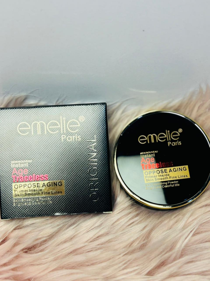 "Emelie Paris Instant Age Traceless compact powder with its box, featuring black and gold packaging placed on a soft pink fur surface."