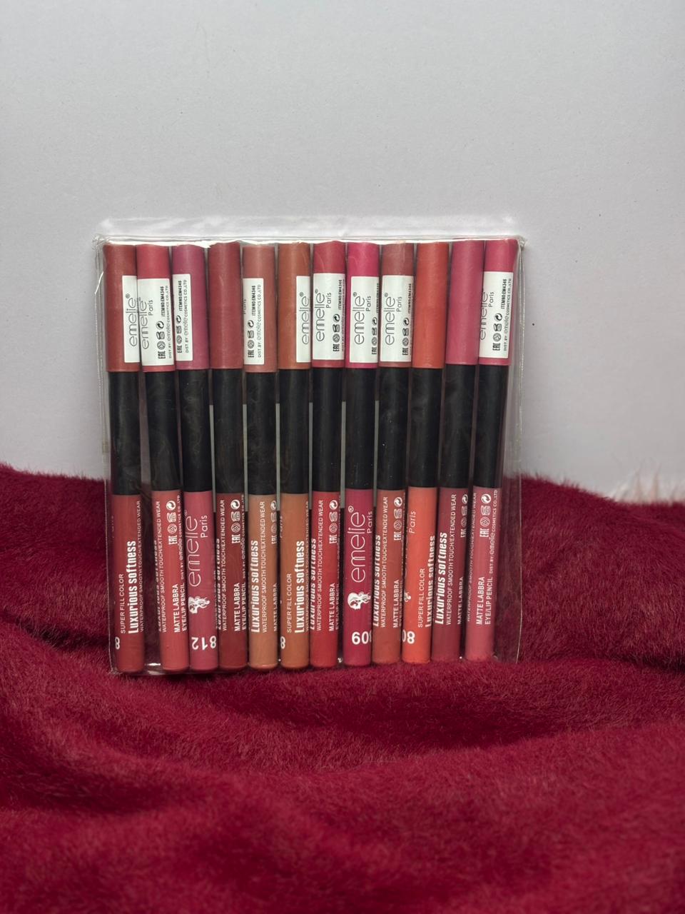 A sealed pack of Emellie matte lip liners in assorted nude, pink, and red shades arranged neatly on a red furry background.