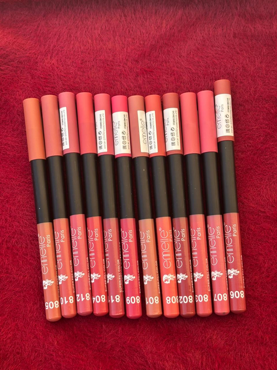 A full set of Emellie matte lip liners spread out in a row, showing various color options on a red furry background.