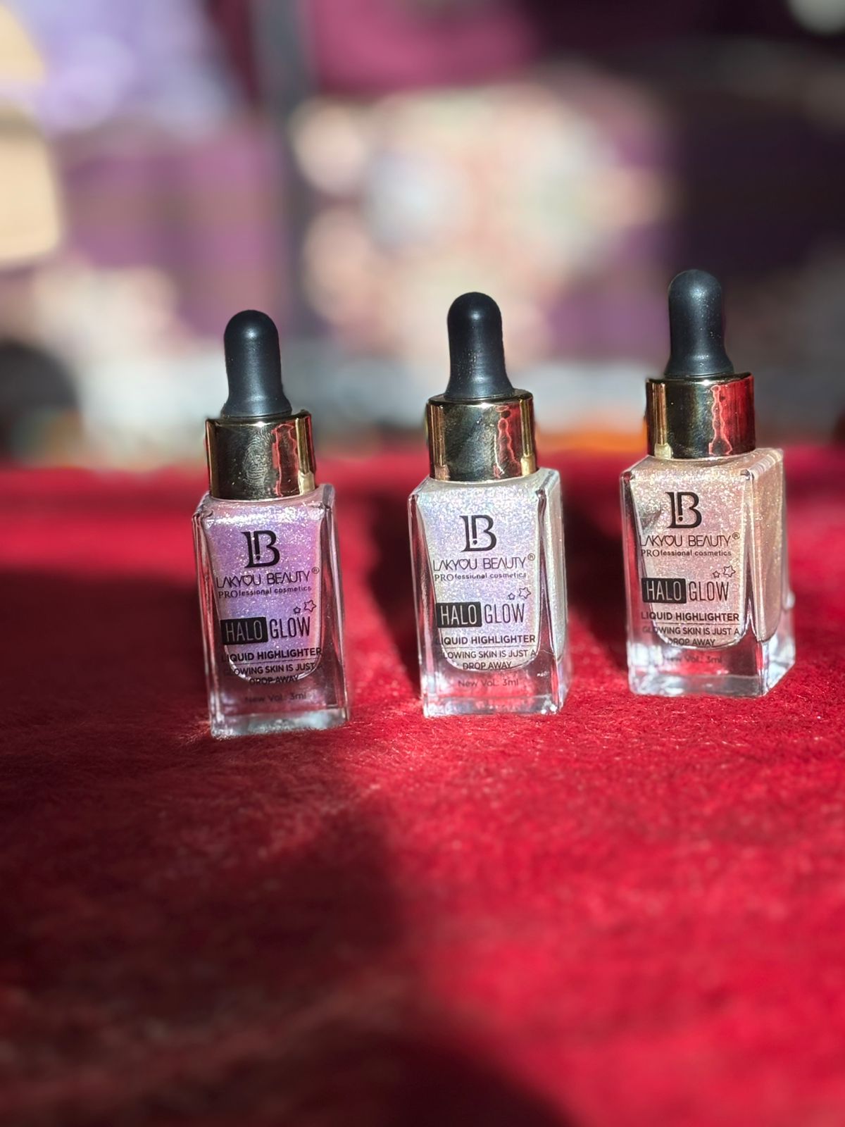 Three makeup glow serum bottles arranged on a vibrant red background with soft sunlight."