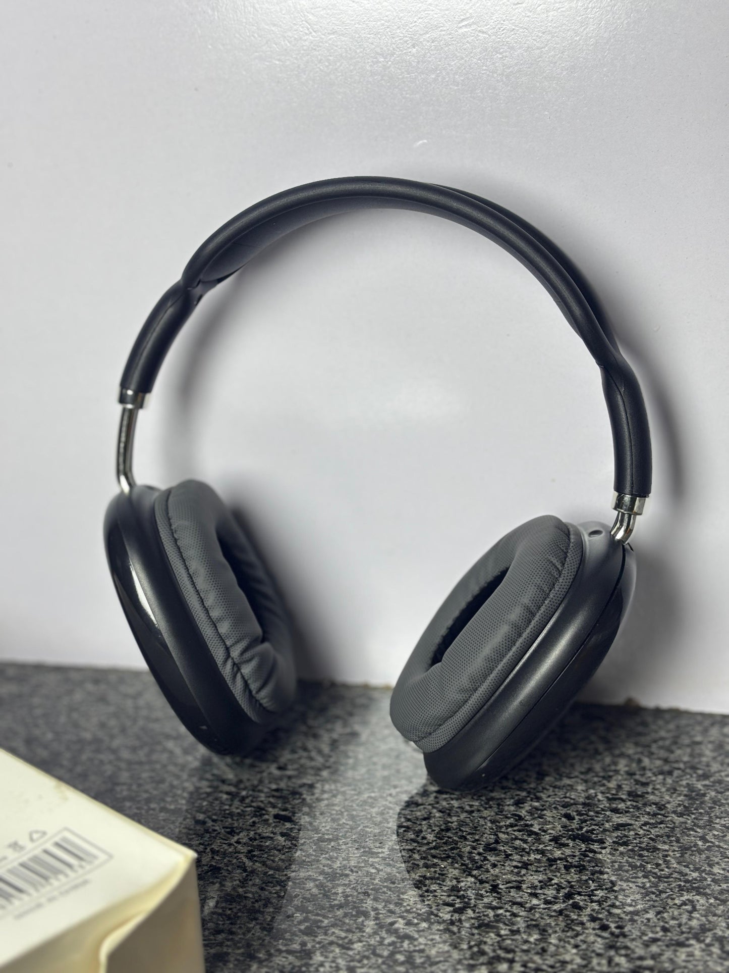 Black wireless over-ear headphones placed on a grey textured surface with product packaging in the background.
