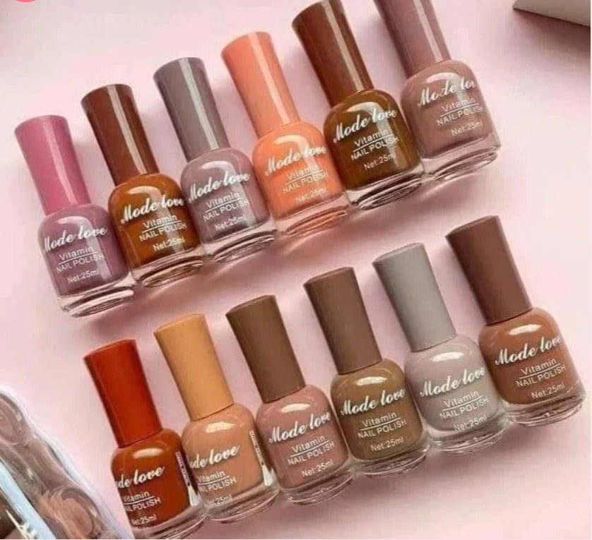A neatly arranged collection of “Mode Love Vitamin Nail Polish” bottles in brown, peach, and nude shades placed on a pink background with nail tools beside them.