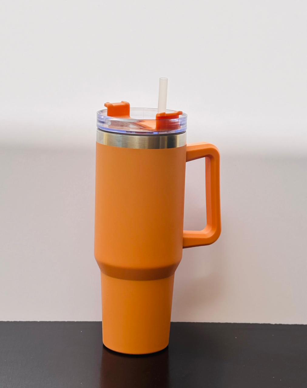 Single orange matte insulated tumbler cup with handle and clear straw placed on a minimal black and white background.