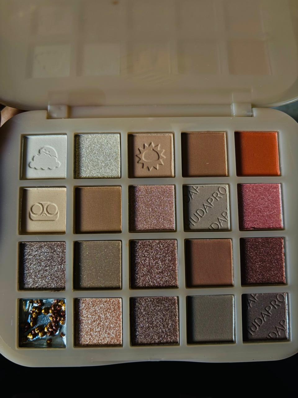 an open HudaPro Chestnut eyeshadow palette showing 20 neutral and shimmer shades with gold and bronze tones.

