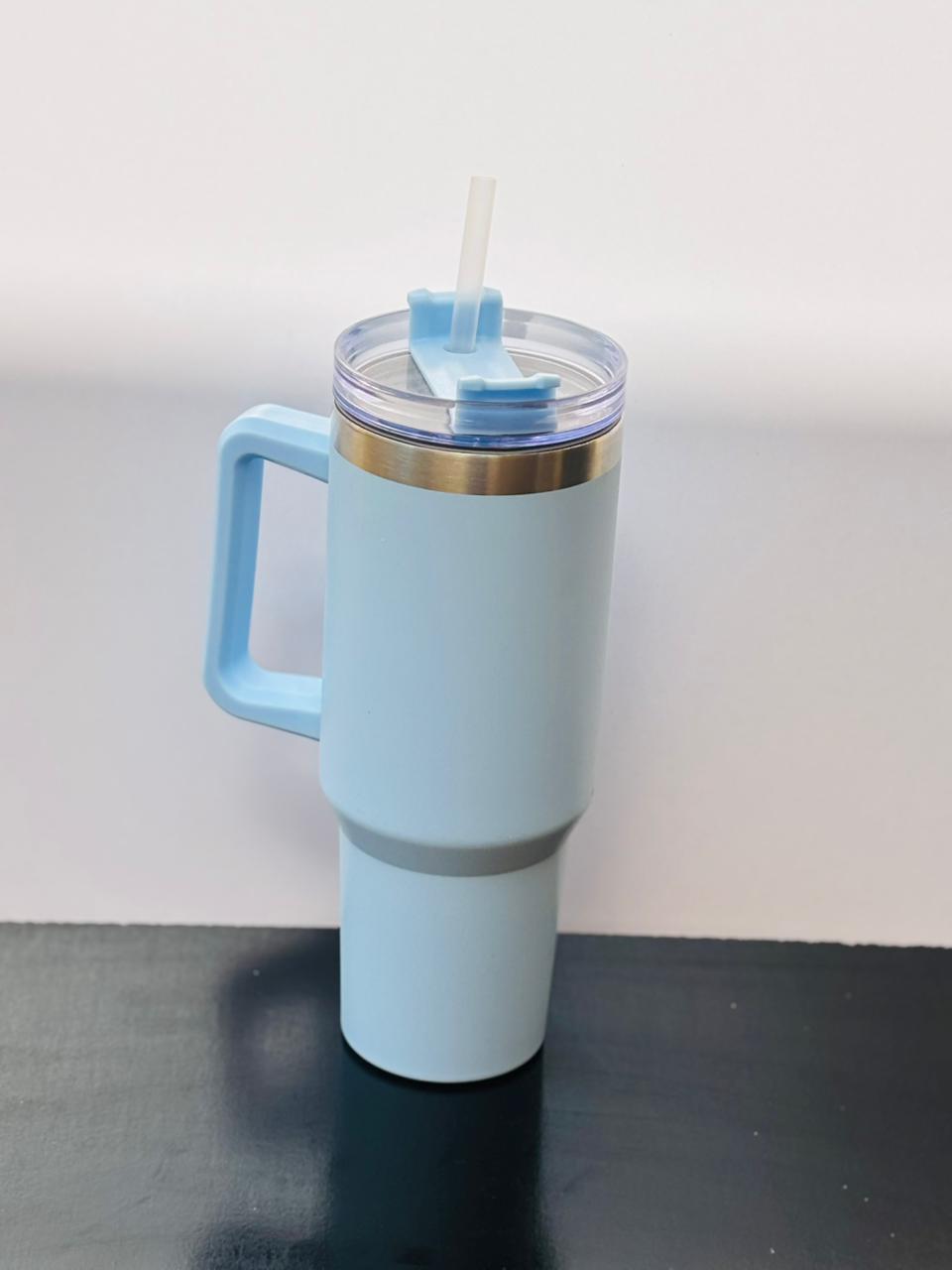 Light pastel blue insulated tumbler cup with handle and straw placed on a black and white surface.