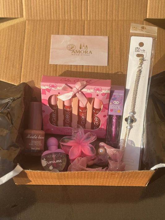 Open cardboard gift box filled with pink beauty items including lip gloss set, nail polish, beauty accessories, and Amora branding