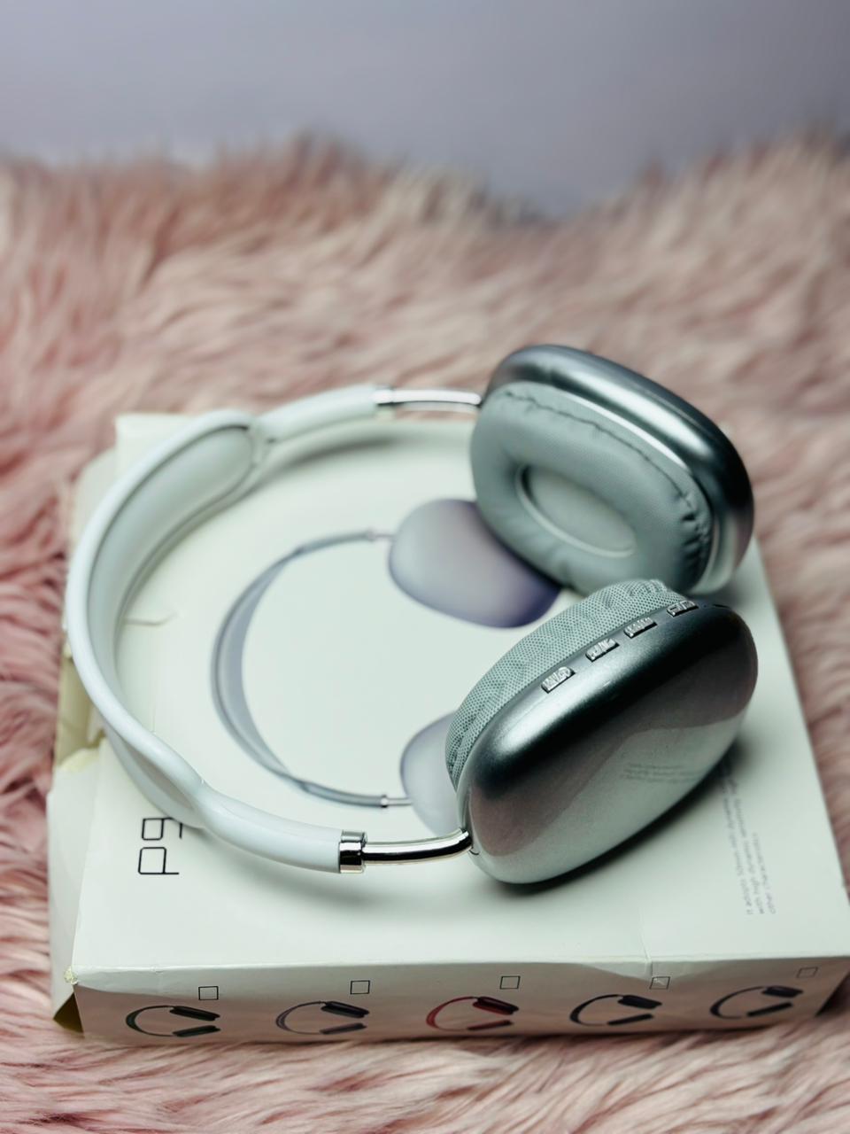 Silver over-ear wireless headphones placed on top of a white product box, displayed on a soft pink background.