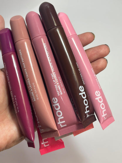 Set of Rhude lip glosses held by a hand on a light background