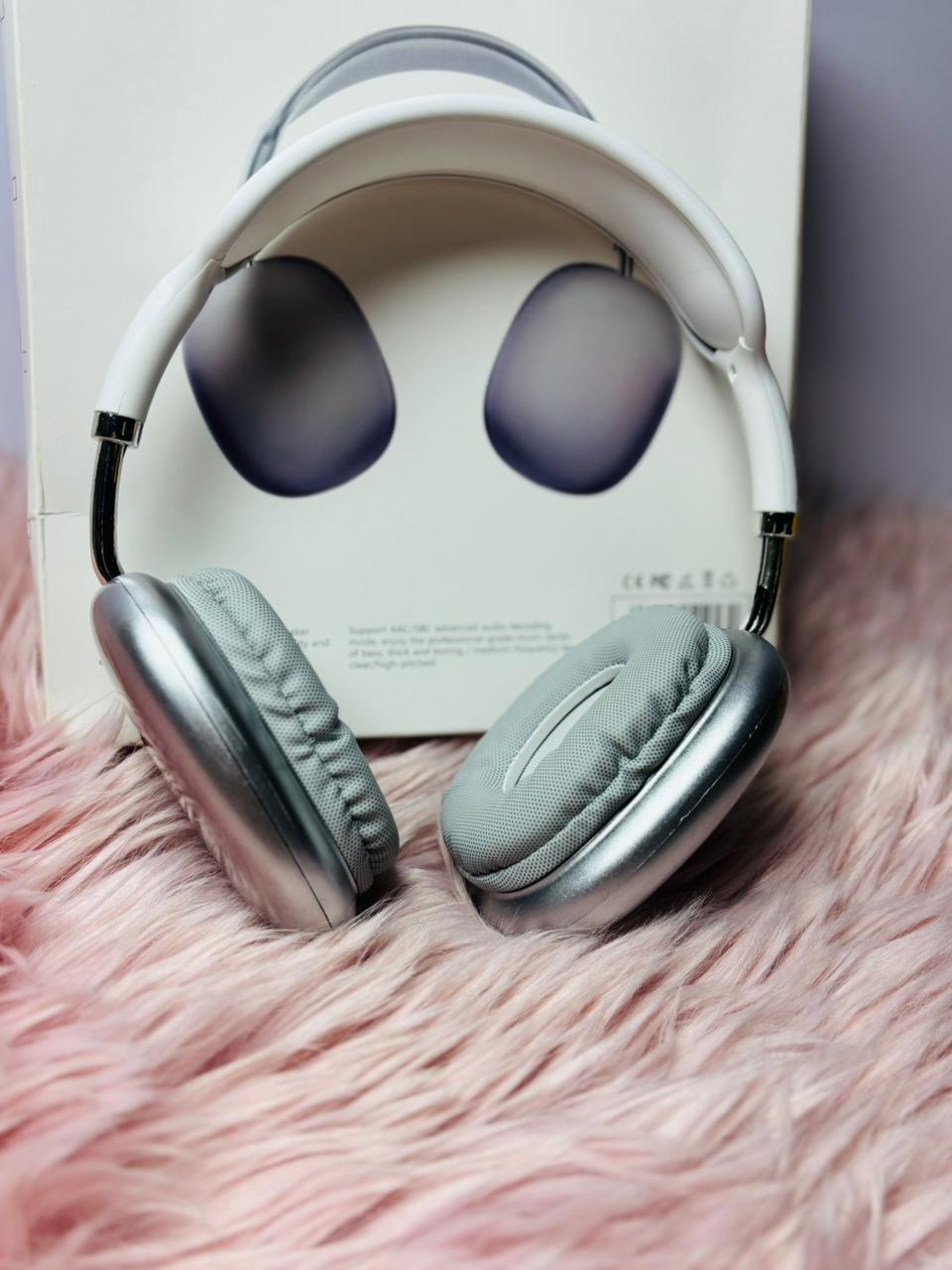 Silver cushioned wireless headphones displayed on a soft pink fur surface with the box shown behind them.