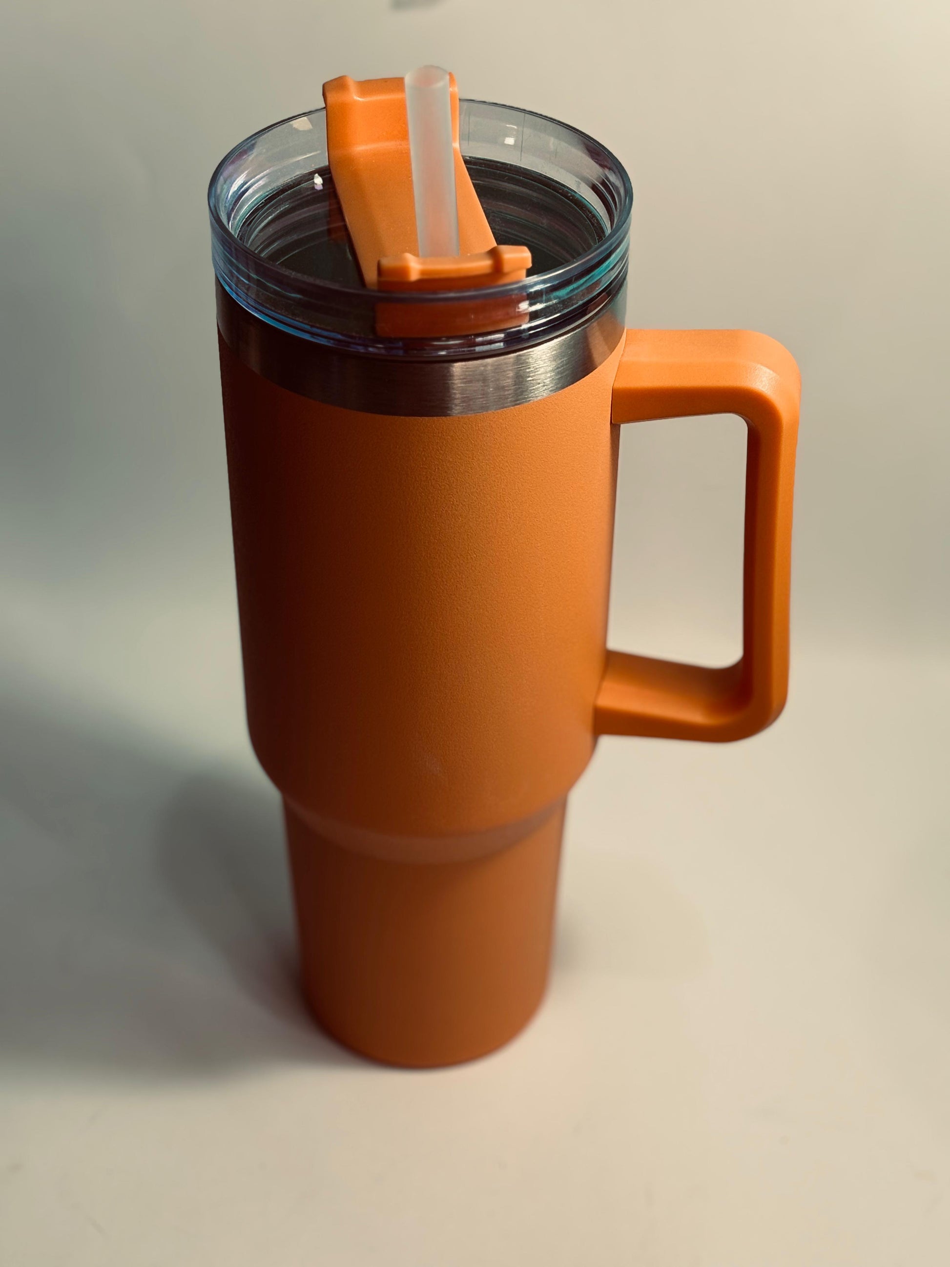 Orange travel mug with a handle and straw on a light gray background