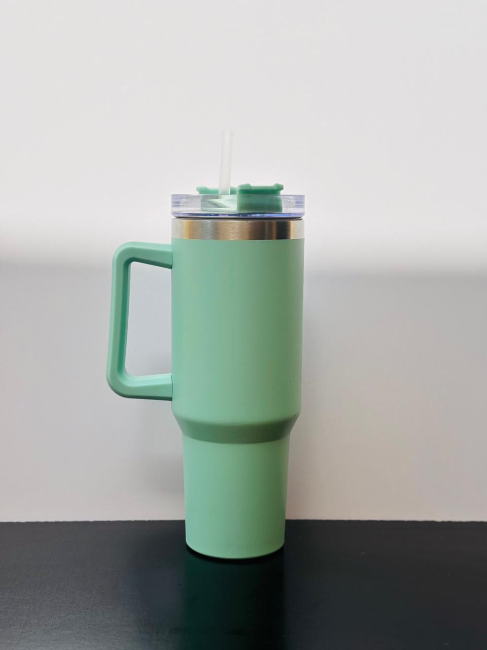 seagreen stainless steel tumbler with a handle and straw placed on a smooth black background.
