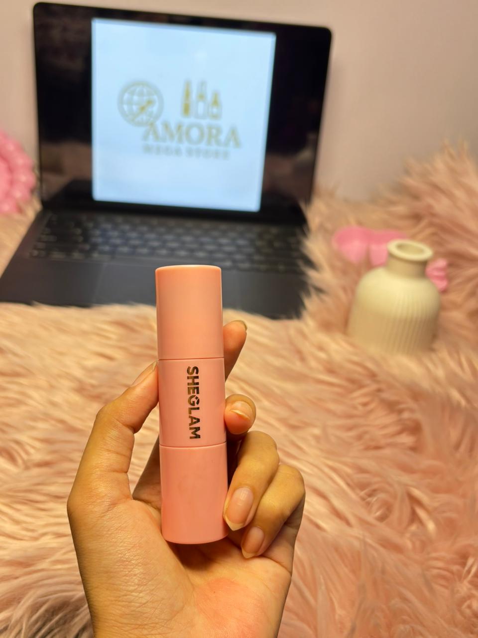 SHEGLAM soft pink liquid blush held in a hand with an Amora Mega Store screen in the background.