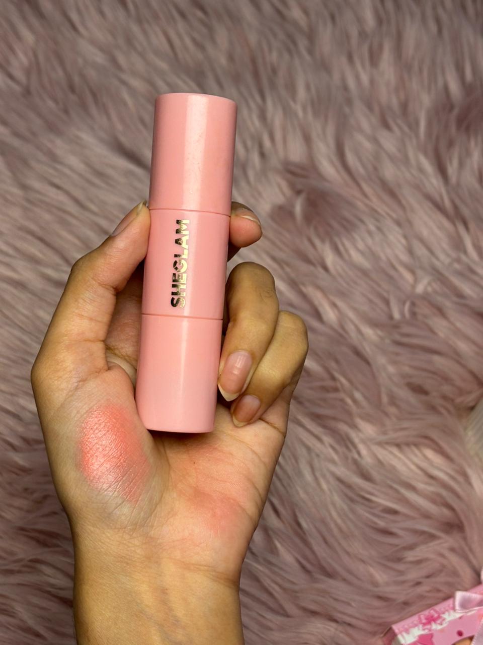 SHEGLAM liquid blush in a soft pink tube held above a pink fur background.
